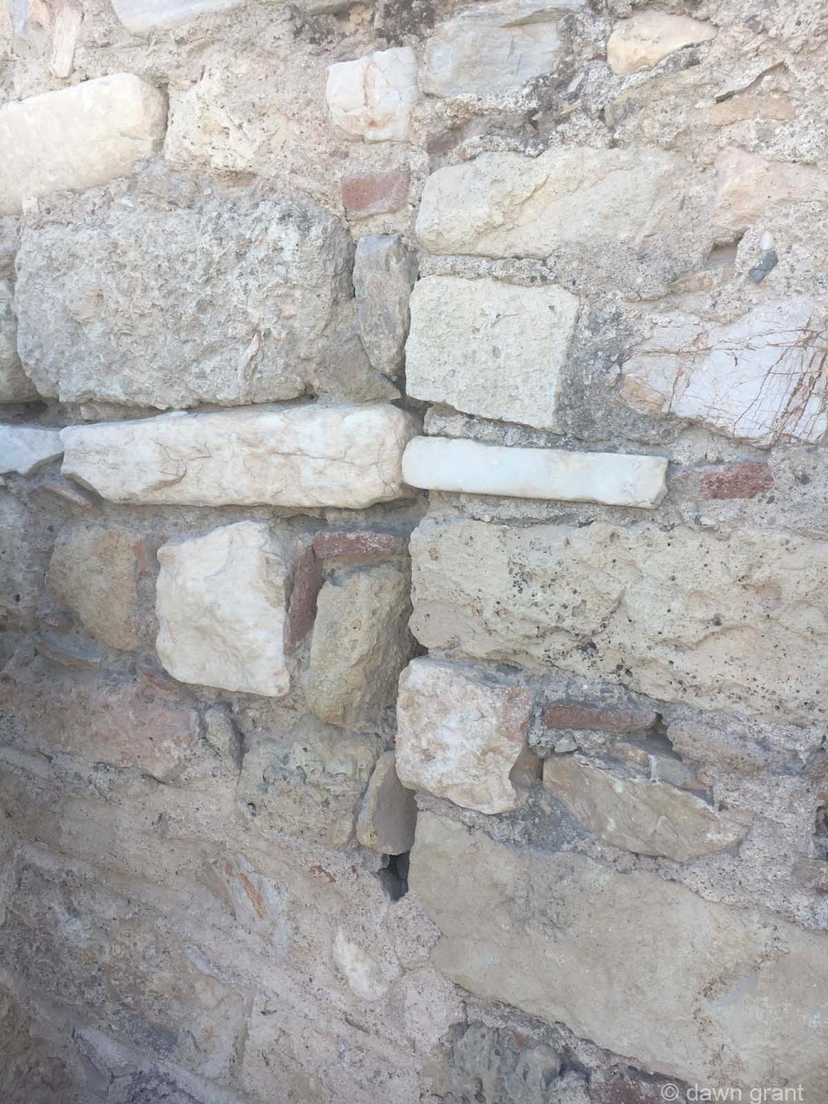 A close up of an old wall made of several different bricks and plaster.