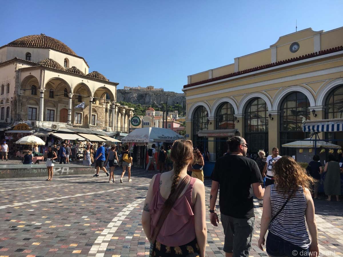 Three people walking across a plaza towards buildings with Mediterranean style on a sunny afternoon.