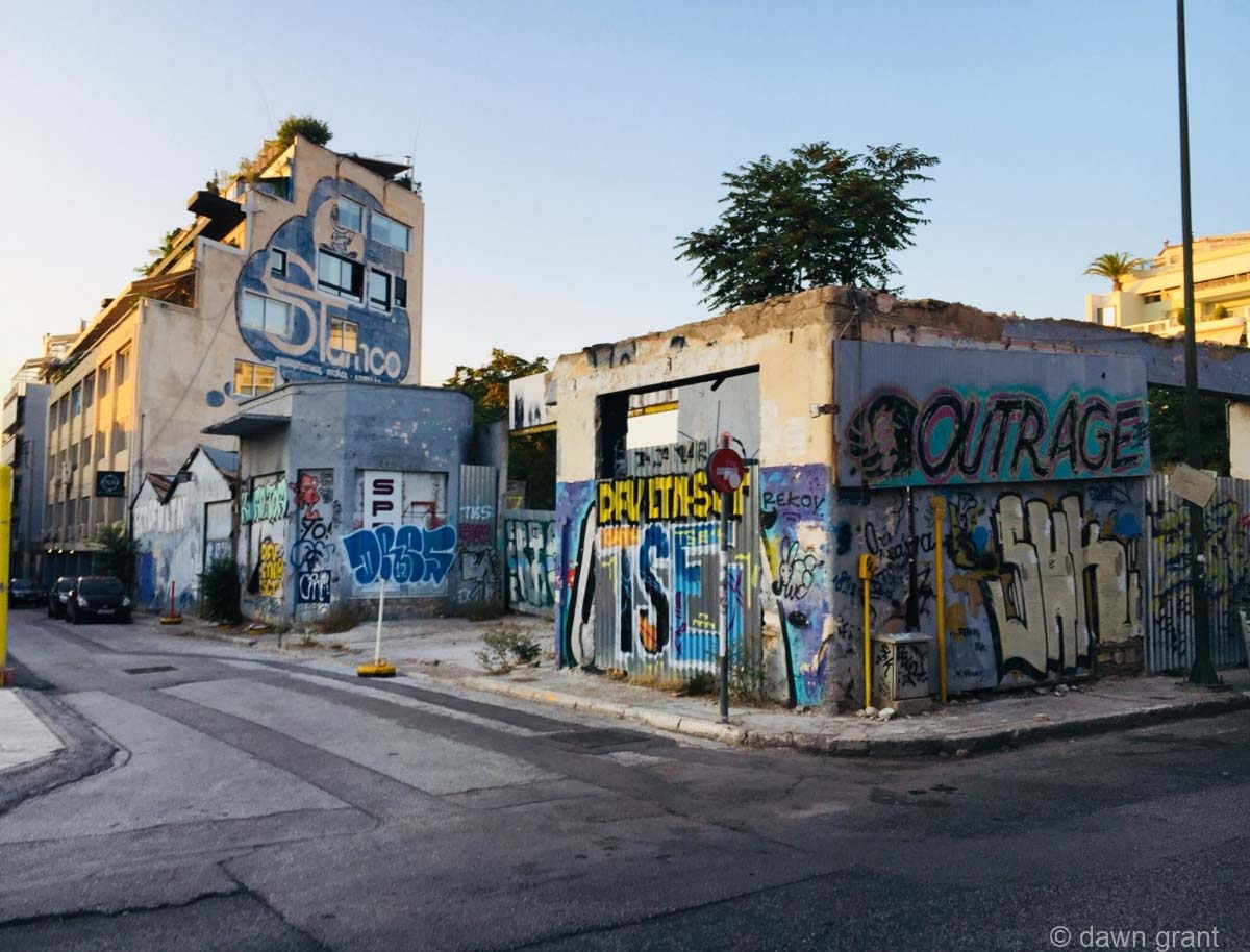 A newer stucco-type building completely covered in mostly-blue graffiti in English and Greek.