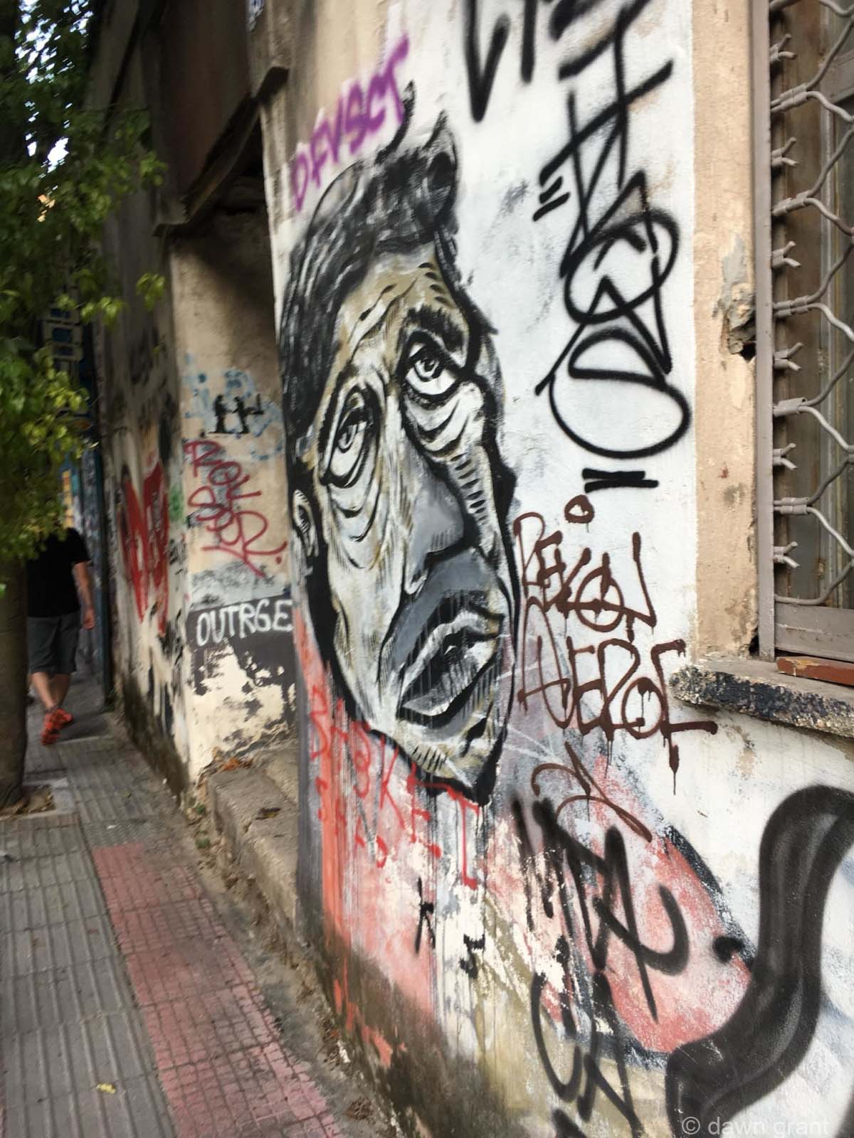 Graffiti spray painted face in black on white concrete, looking up with words coming out of his mouth.
